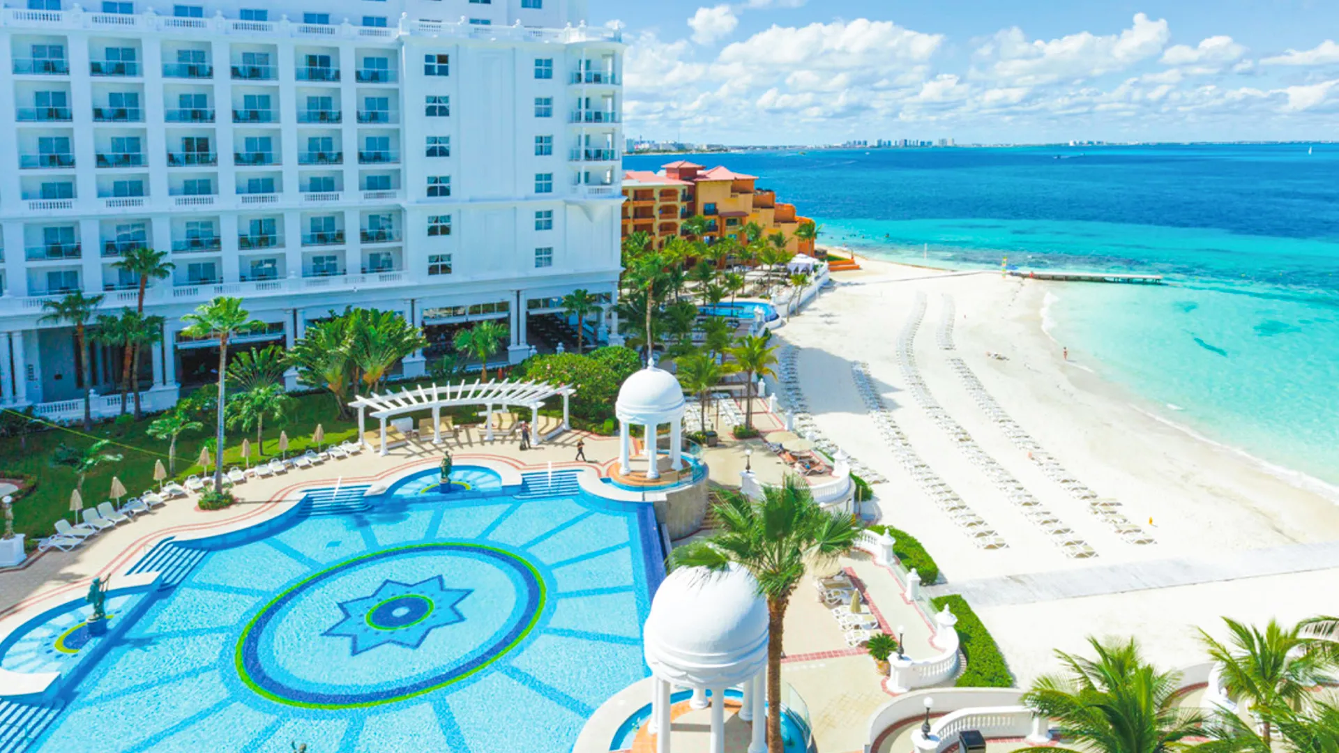  Aerial view of Riu Palace Cancun’s infinity pool and private beach overlooking turquoise Caribbean waters. 