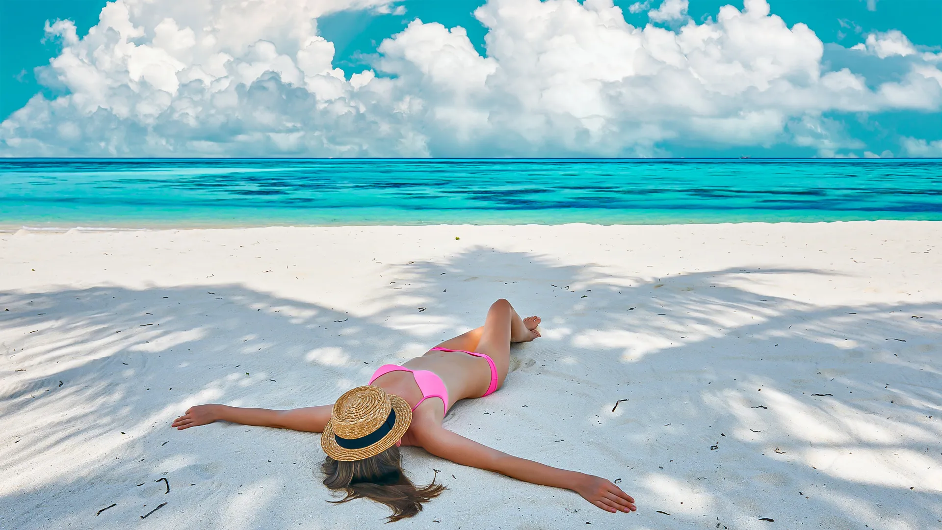 Woman in a pink bikini relaxing on a tropical white-sand beach under palm shadows with turquoise ocean and clouds in the distance