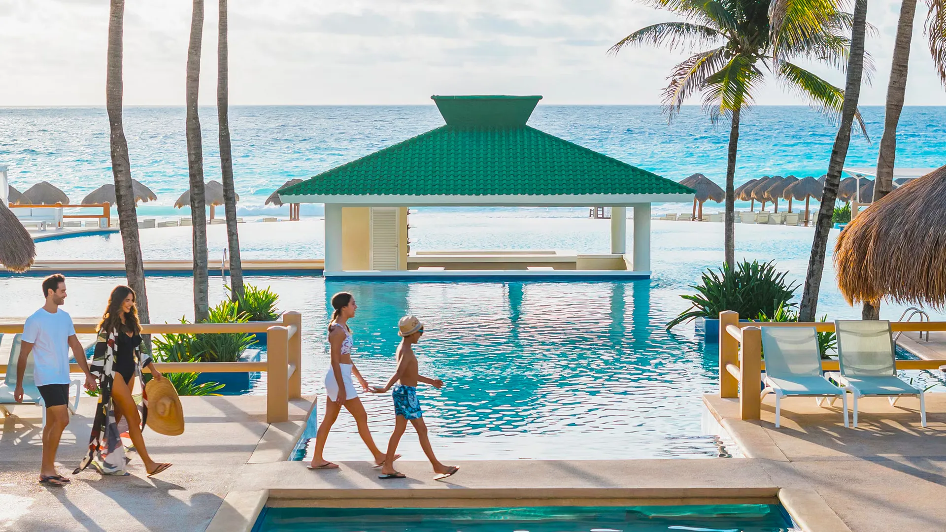 Family walking by the poolside with ocean views at Iberostar Cancun resort.