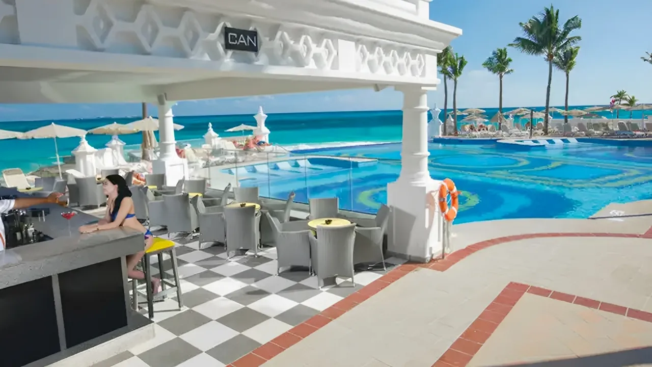  Guest enjoying a drink at the oceanfront pool bar with turquoise water views at Riu Palace Cancun. 