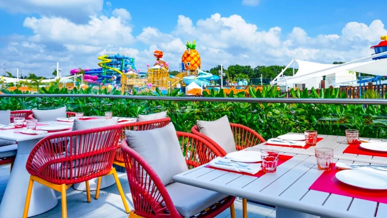 Colorful outdoor dining terrace at Nickelodeon Resort Cancun overlooking Aqua Nick waterpark and SpongeBob’s pineapple house.
