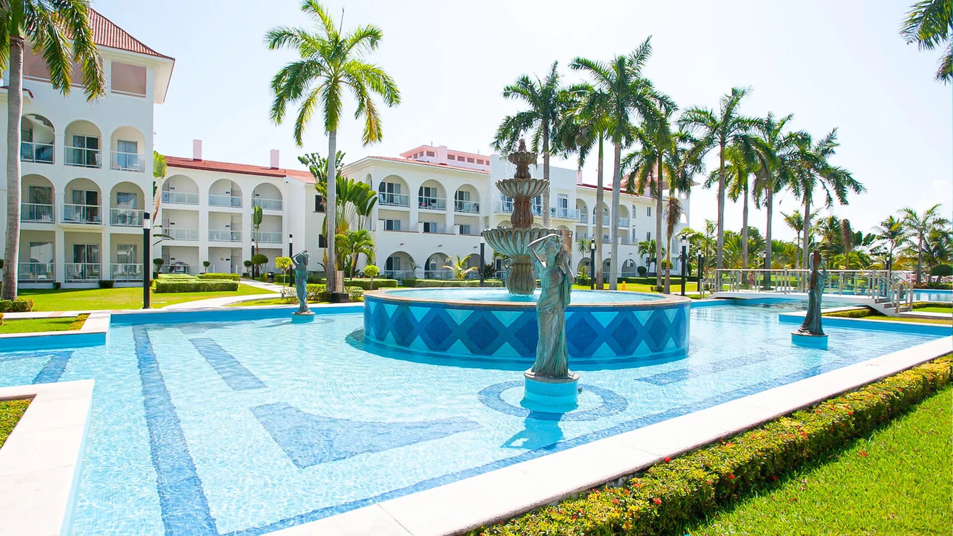 Elegant courtyard at Riu Palace Cancun featuring palm trees, statues, and a central blue-tiled fountain.