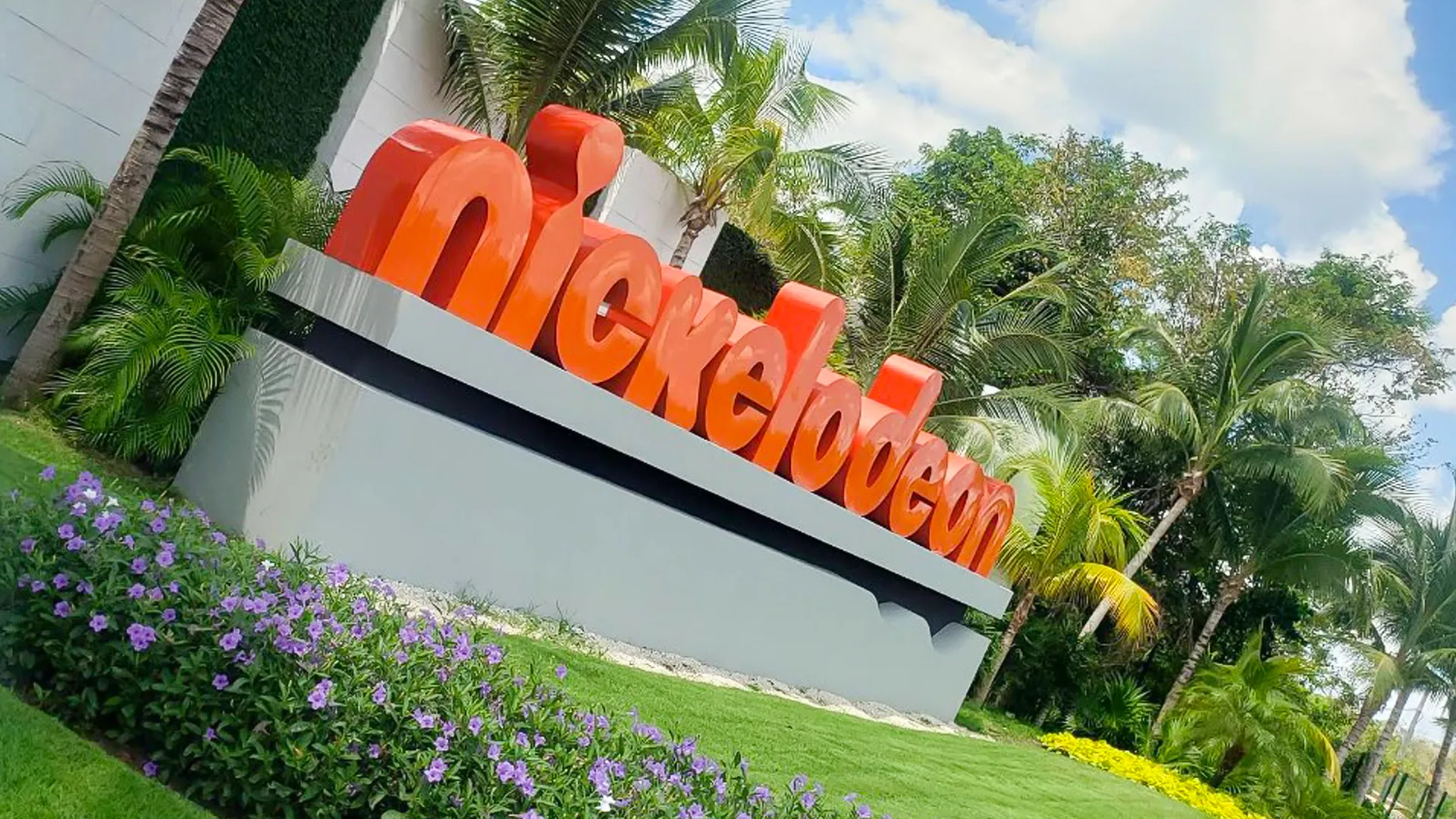 Large orange Nickelodeon sign surrounded by tropical palm trees at the entrance of Nickelodeon Resort Cancun. 