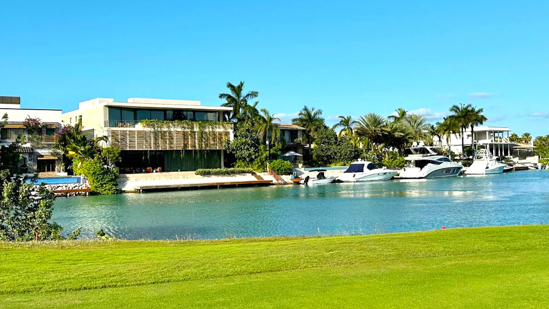 Modern waterfront villas with yachts docked along a calm turquoise canal under clear blue skies.