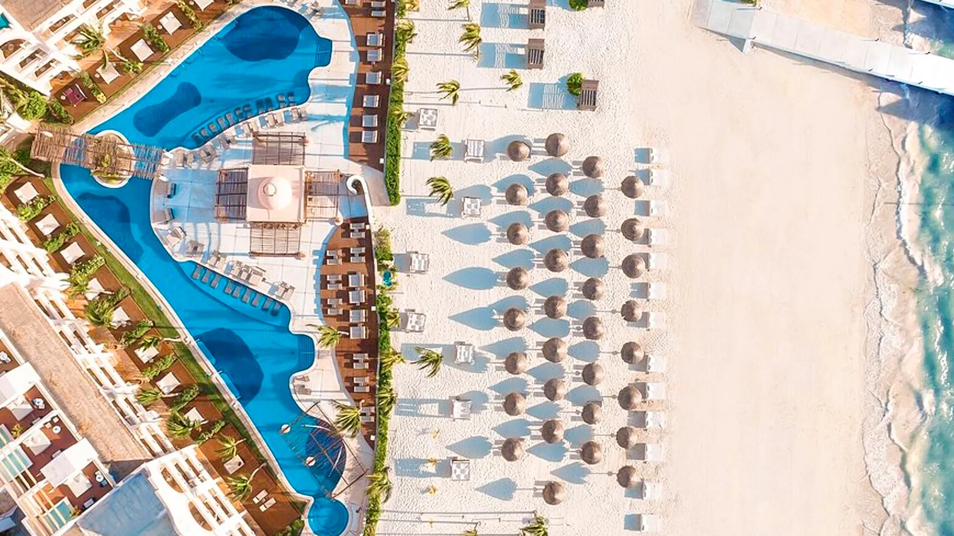 drone shot of resort pools, palapas, and white sandy beach