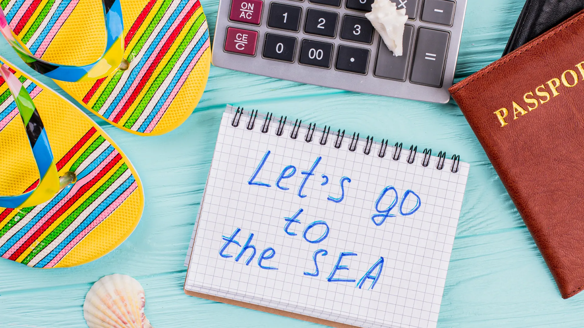 Summer flat lay with colorful flip-flops, seashells, passport, and note reading “Let’s go to the sea.”