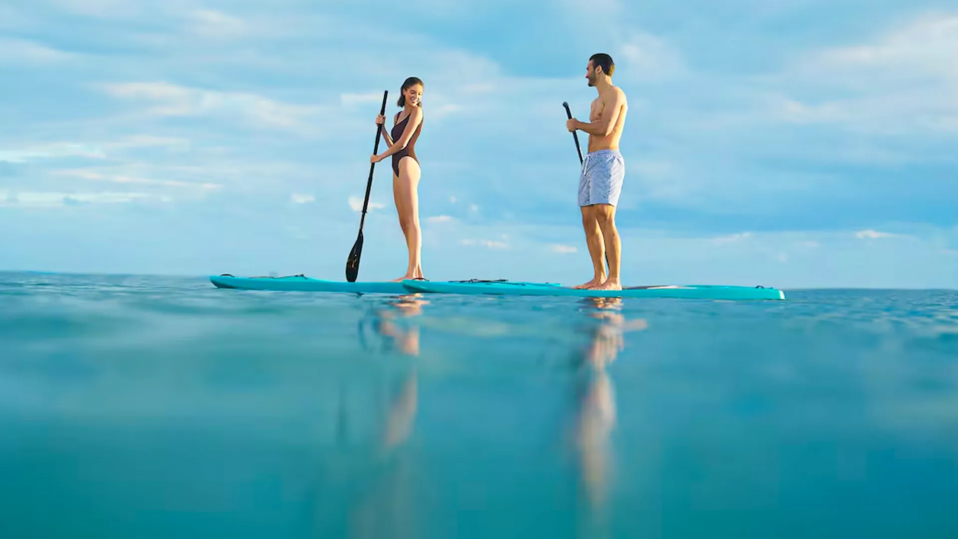 Couple paddleboarding on the turquoise Caribbean waters at Hilton Cancun resort under a bright sky.