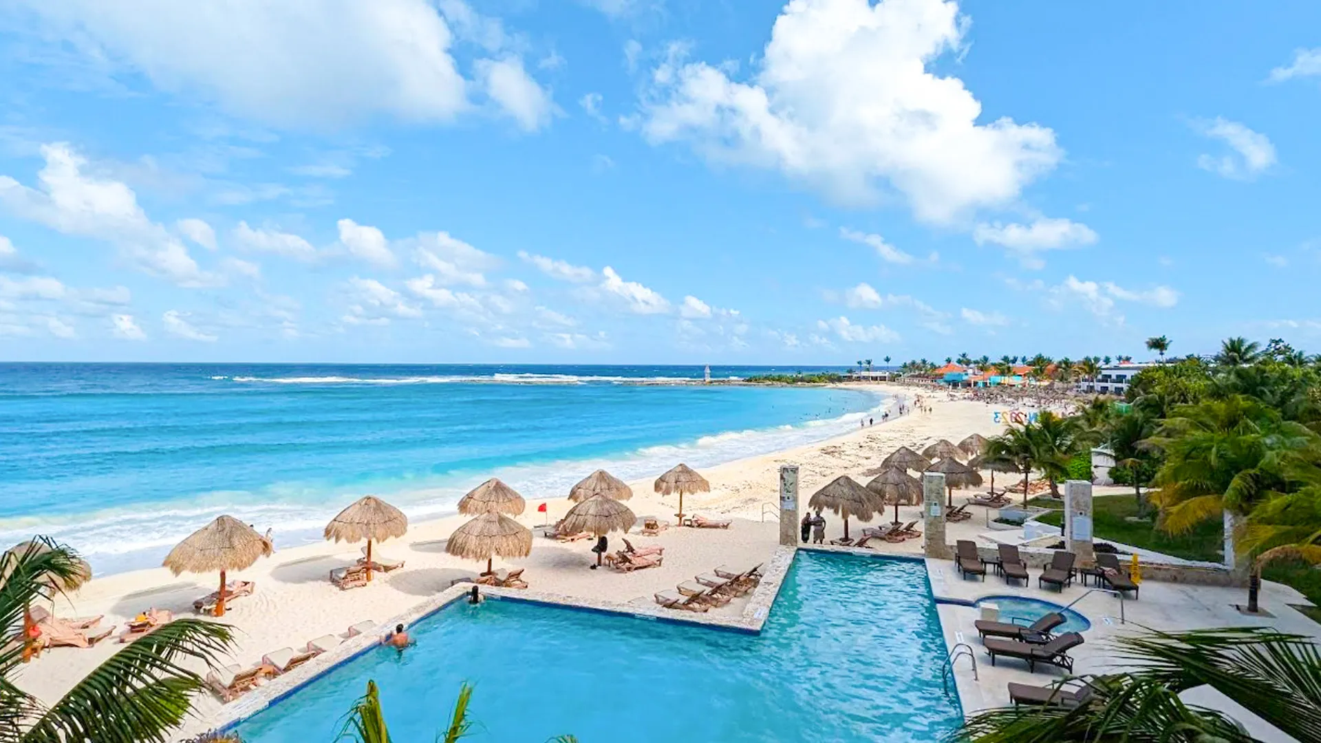 Aerial view of beachfront resort with palm-fringed pools, sun loungers, and turquoise Caribbean sea.