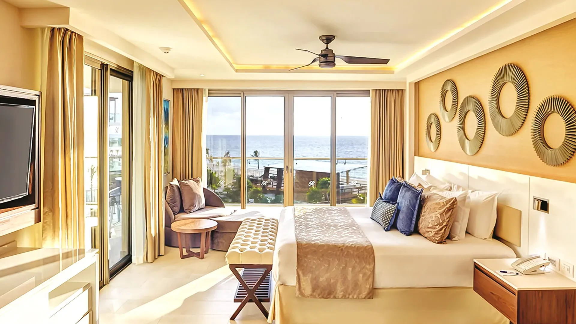 Luxury ocean-view suite at Royalton Riviera Cancun with golden accents, large bed, and floor-to-ceiling windows overlooking the sea.