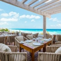 Outdoor dining terrace at Oleo Cancun Playa with ocean views, wooden pergola, and set tables overlooking turquoise waters.