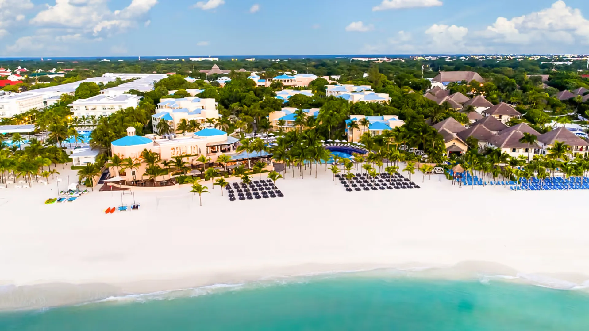 Aerial shot of the Royalton Riviera Cancun resort surrounded by palm trees, white sand beach, and clear turquoise sea.