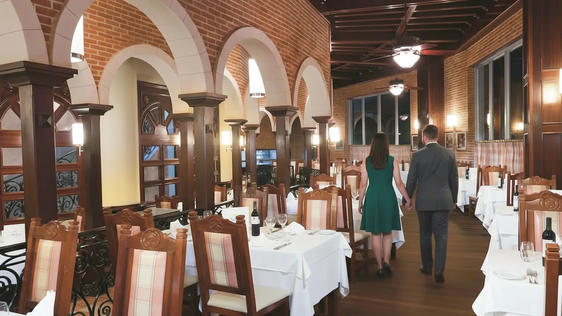 A couple walking hand in hand through a warmly lit dining room with arched brick walls, wooden tables, and elegant chairs