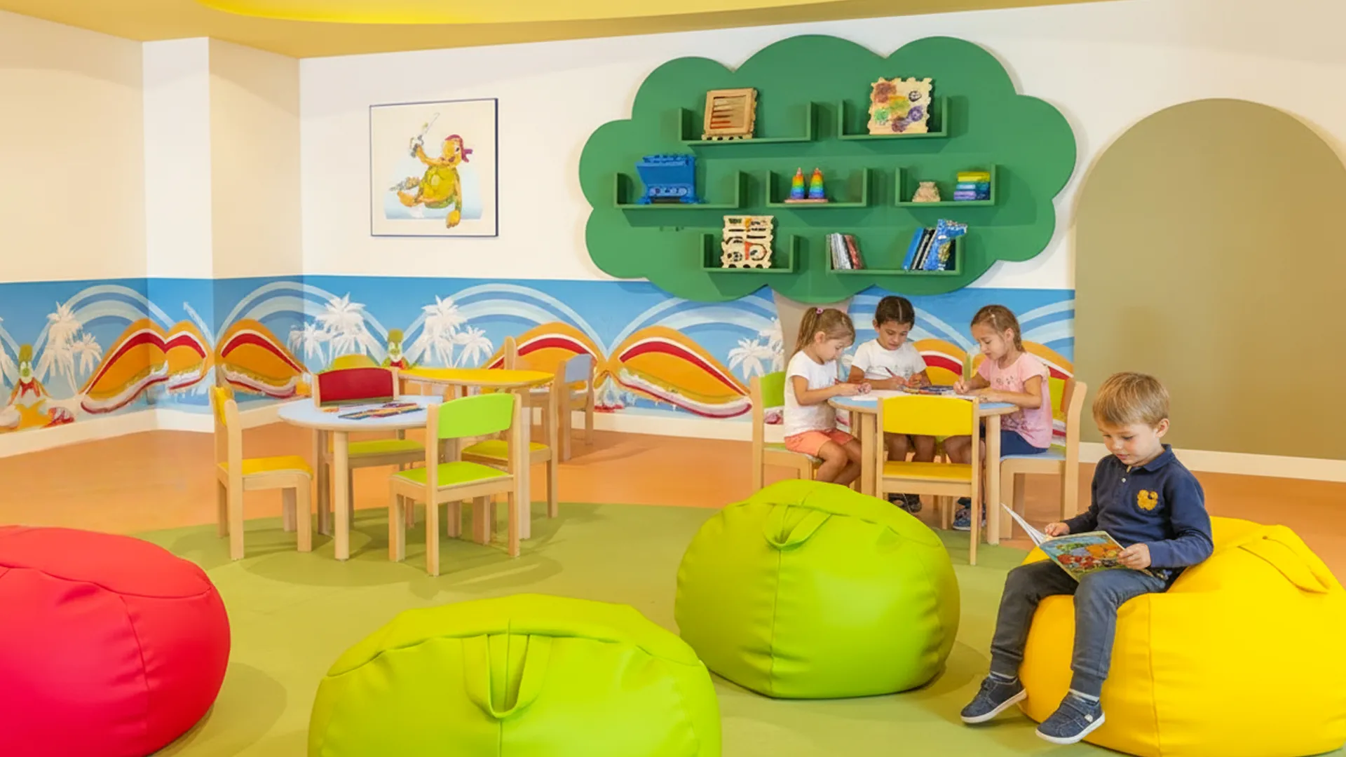 A colorful kids' playroom with a green tree-shaped bookshelf, small tables, and chairs in yellow and red, children engaged in activities, and large bean bags in red, green, and yellow on a green carpeted floor, featuring a tropical-themed wall mural.