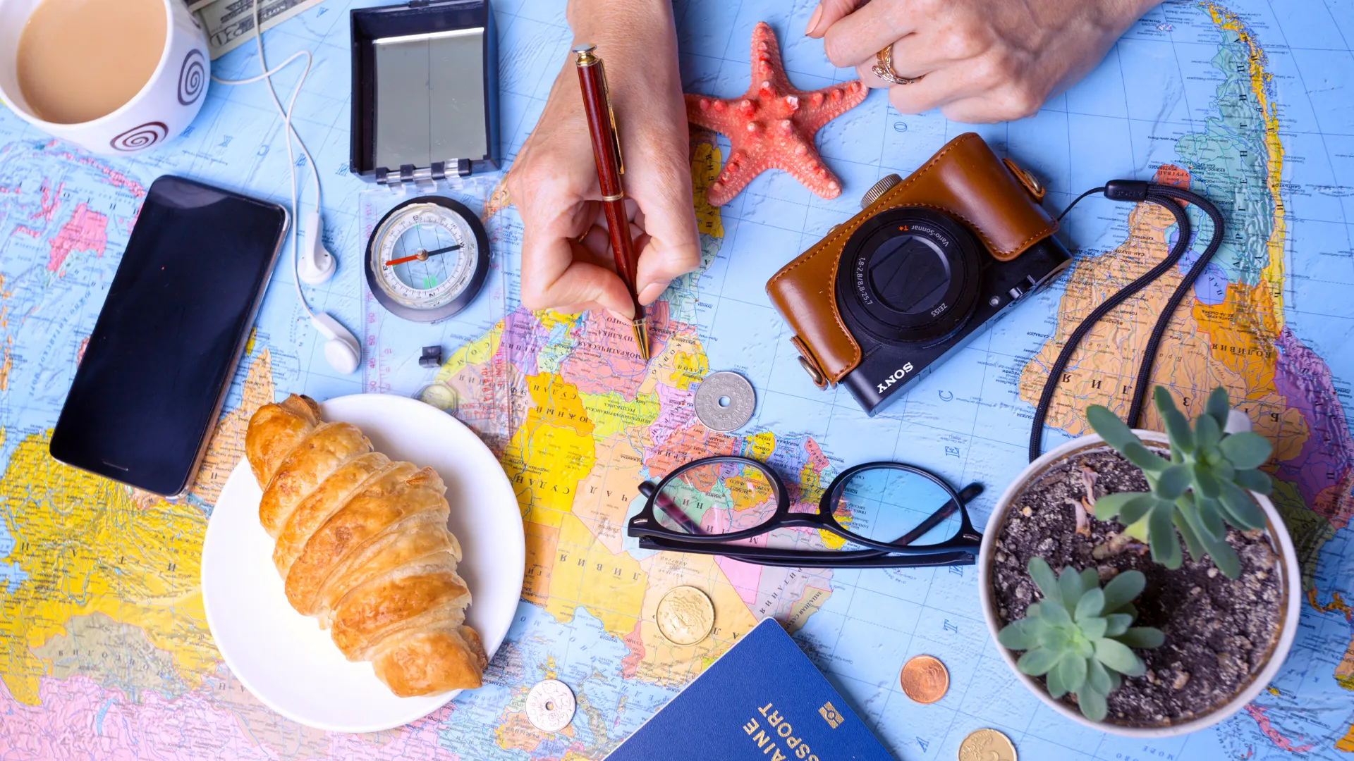 Travel planning essentials laid out on a world map with a camera, passport, croissant, and coffee before a trip to Riu Caribe Cancun.
