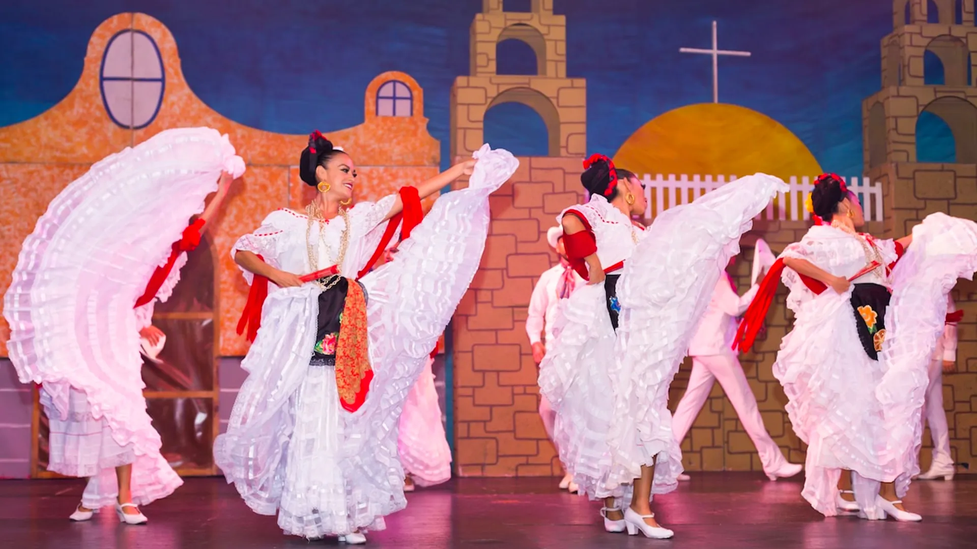 Traditional dance performance at the GR Solaris Cancun resort with dancers in white dresses with red accents, twirling large white skirts, and a backdrop of a painted Mexican village scene.