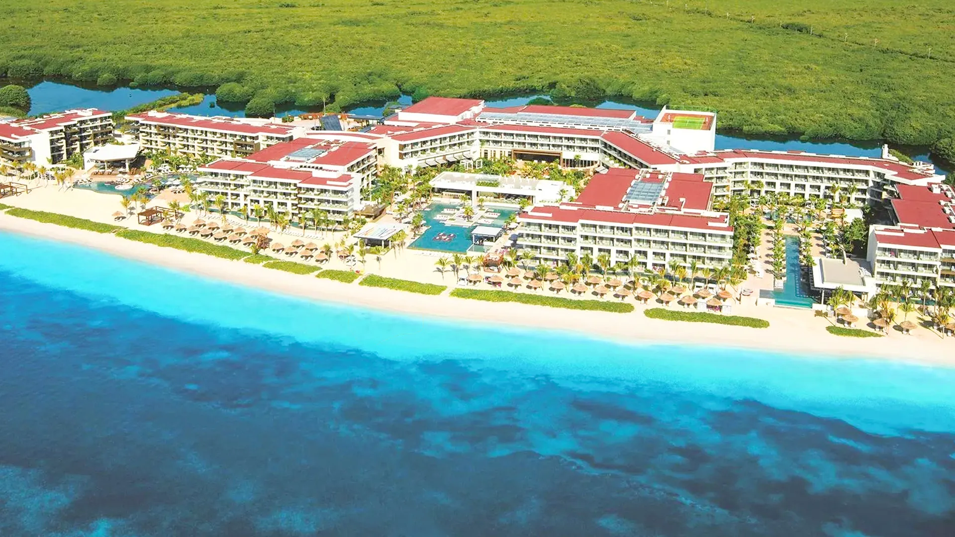 Aerial view of Breathless Riviera Cancun Resort showing pools, palm trees, and beachfront along the Caribbean Sea.