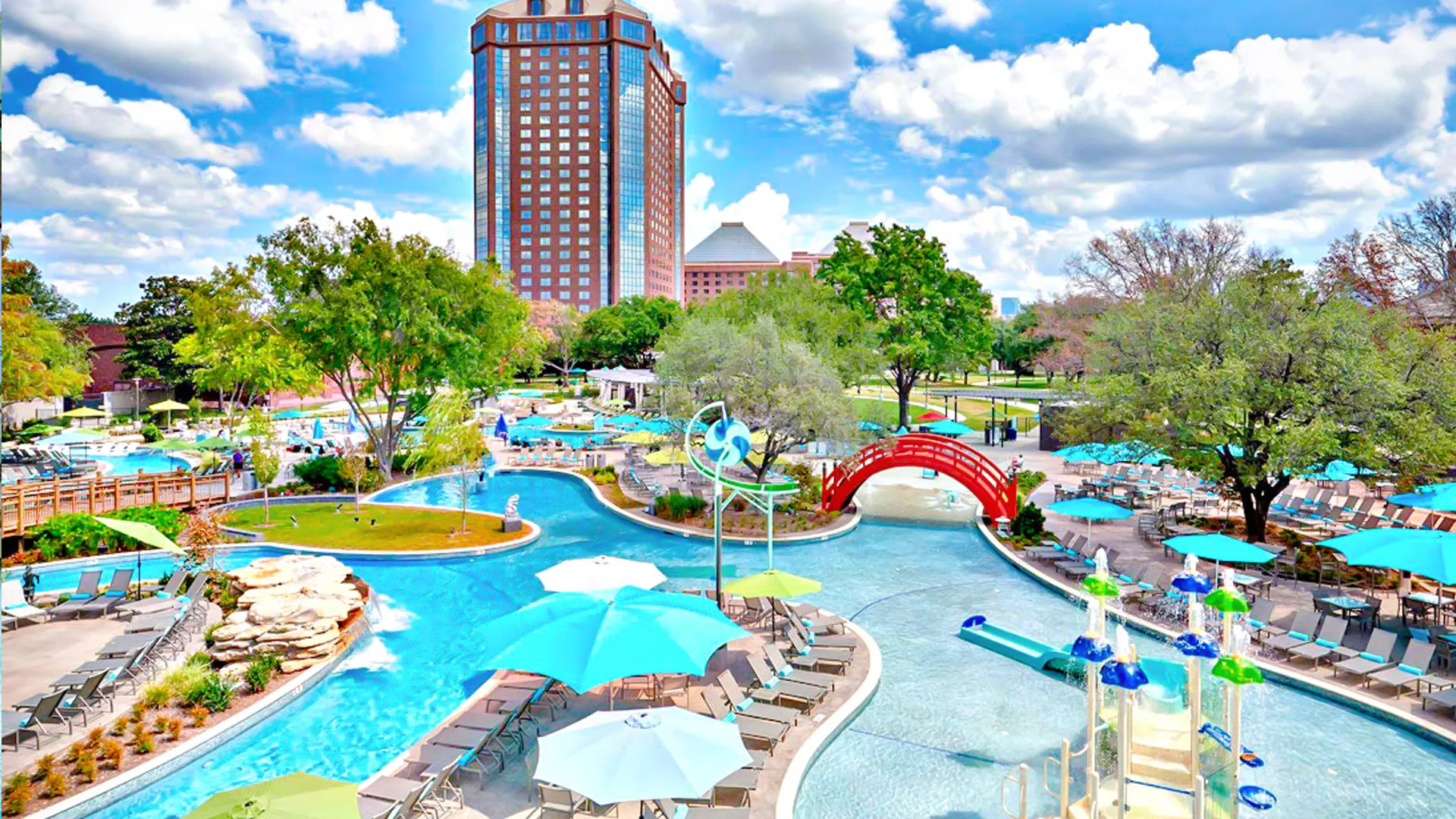 Aerial view of Hilton Cancun resort with a lazy river, pool area, red bridge, and lush tropical gardens under a bright blue sky.