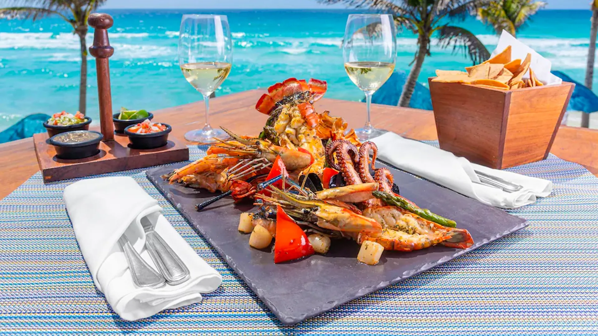  A delicious seafood platter served with wine glasses by the beach, showcasing Grand Oasis Cancun's diverse dining options.