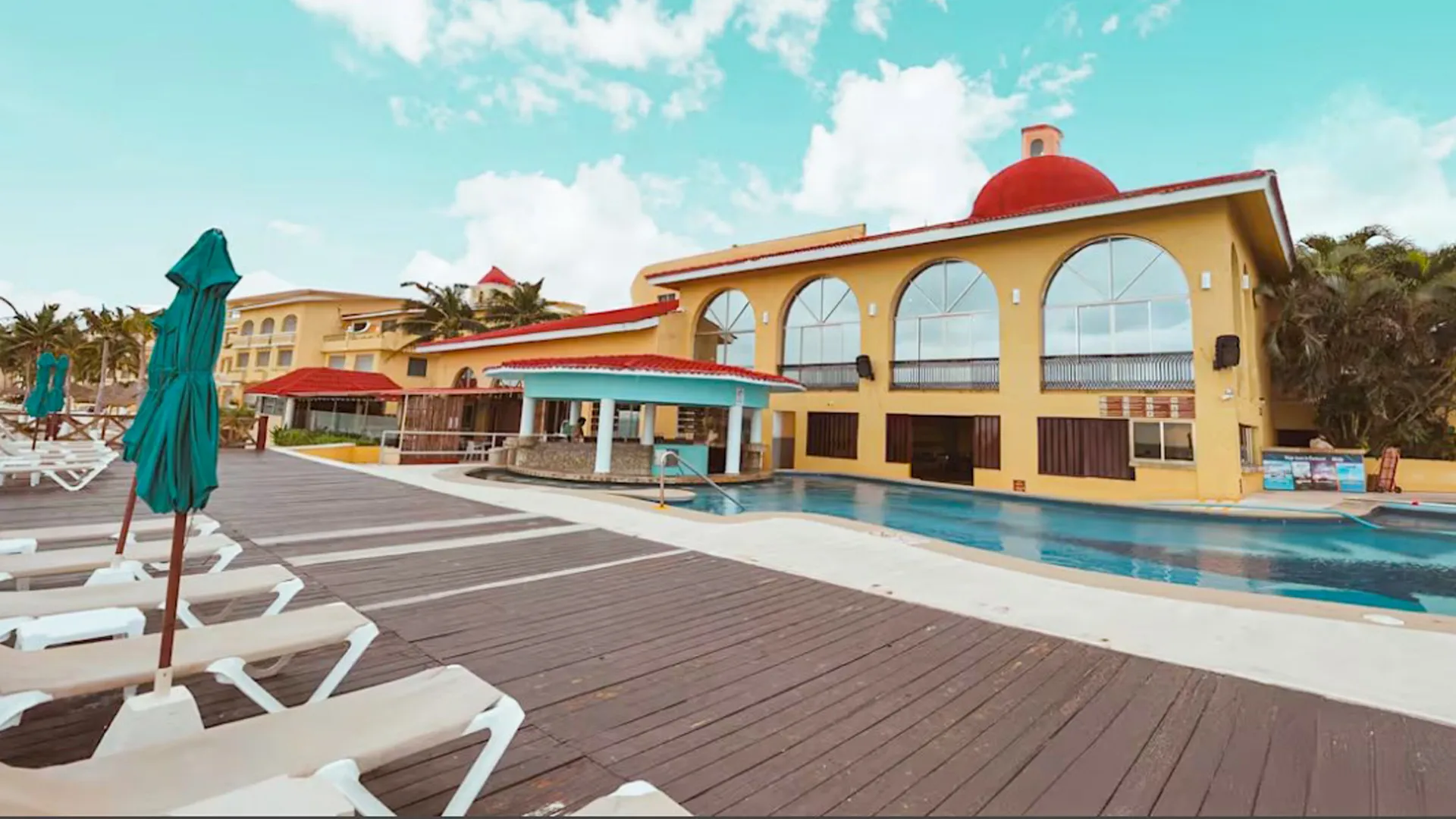 Outdoor pool and sun deck at All Ritmo Cancun Resort with lounge chairs and pool bar under the red dome building.