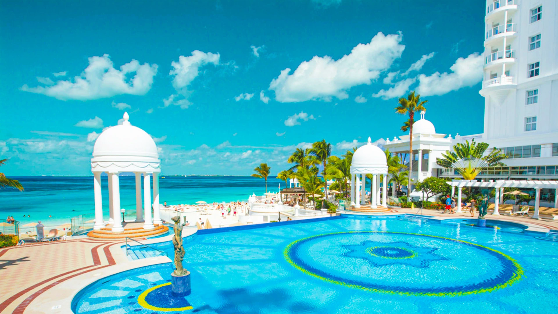 Aerial view of Temptation Cancun Resort’s main pool with white domes, palm trees, and turquoise Caribbean Sea backdrop.