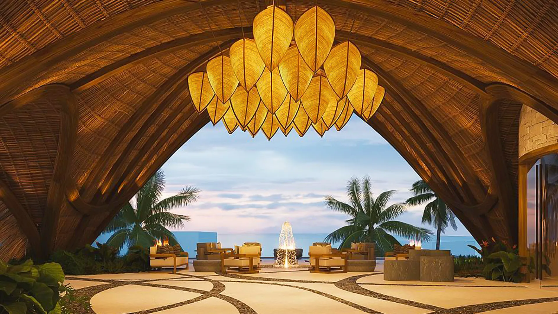 A stunning open-air lounge with a thatched archway roof, leaf-shaped hanging lanterns, comfortable seating around a central fountain, surrounded by palm trees and lush greenery with an ocean view at dusk.
