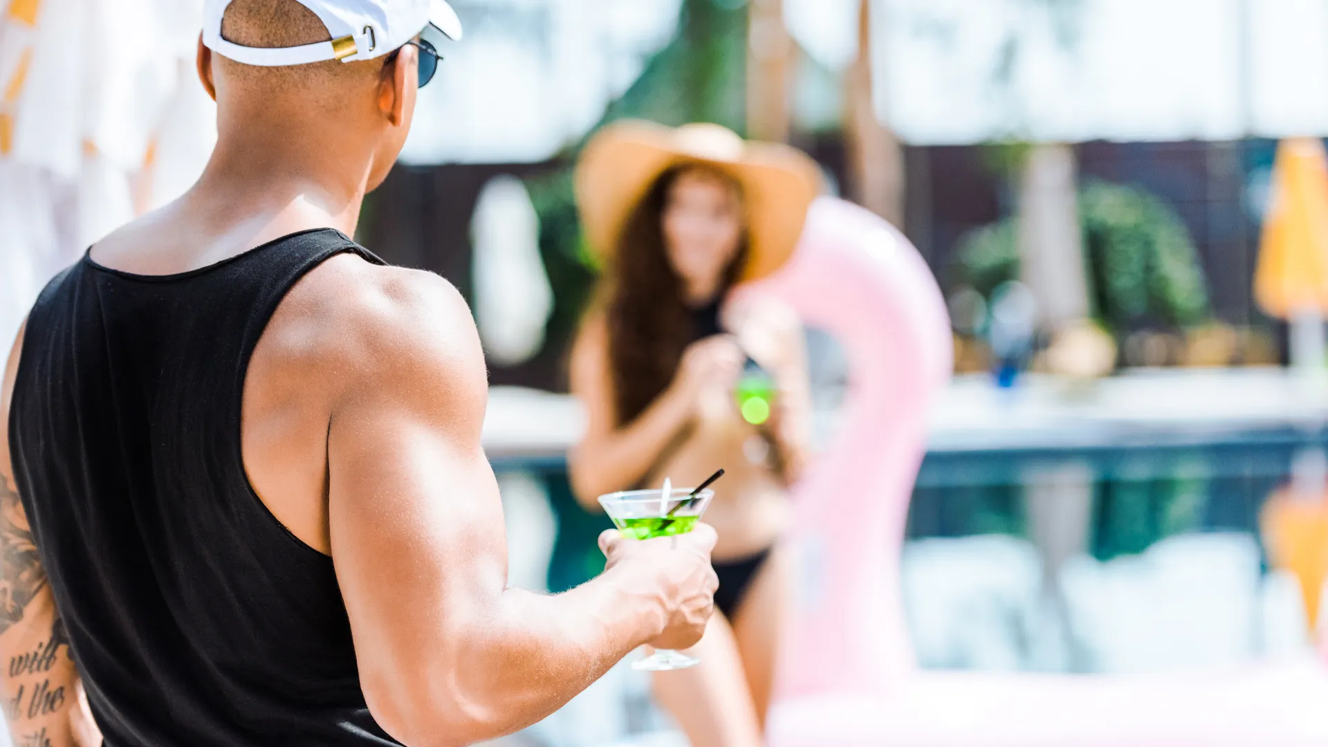 Man and woman holding cocktails by the pool at Hotel NYX Cancun, with tropical background and relaxing resort vibe.