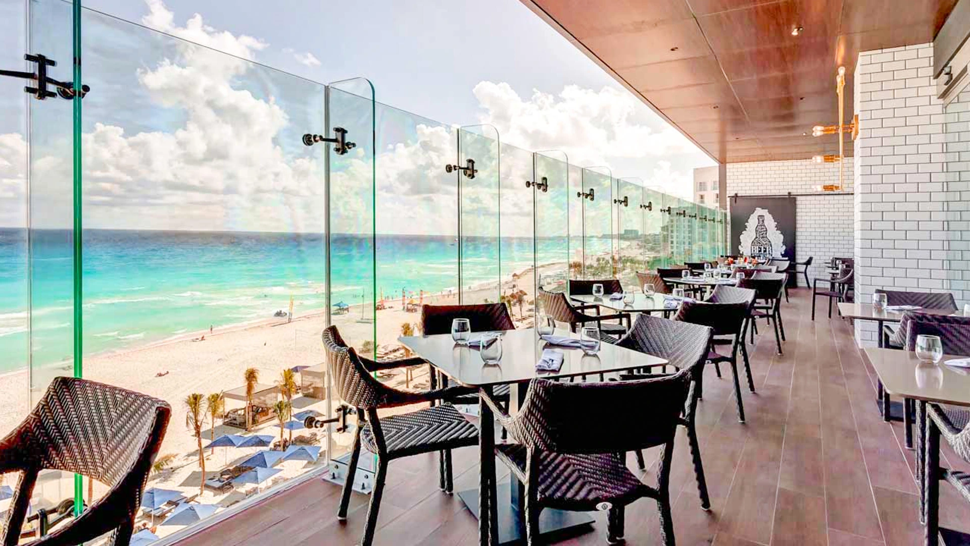 Ocean-view terrace restaurant at Royalton Chic Cancun with modern glass railings and turquoise sea in the background.