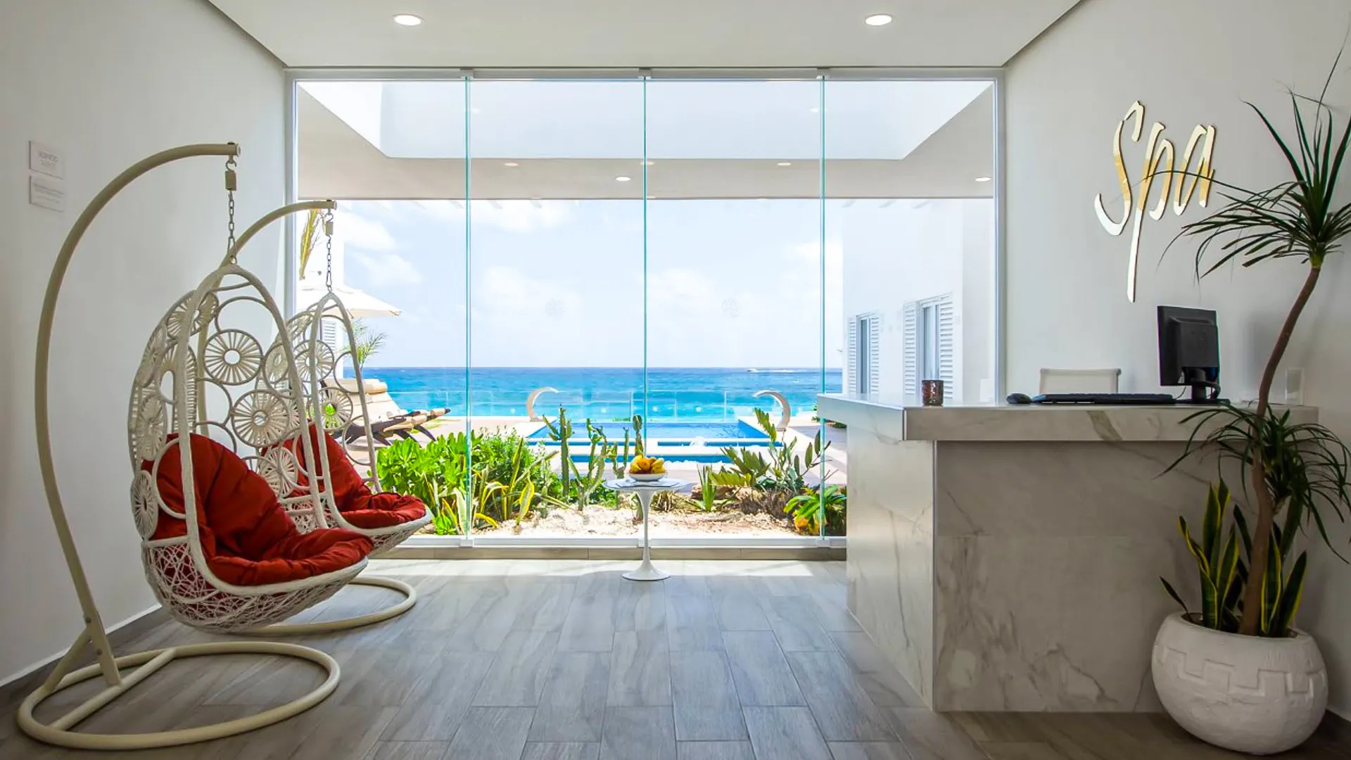 Spa reception at Oleo Cancun Playa with ocean-view glass wall, hanging chairs, and minimalist décor.