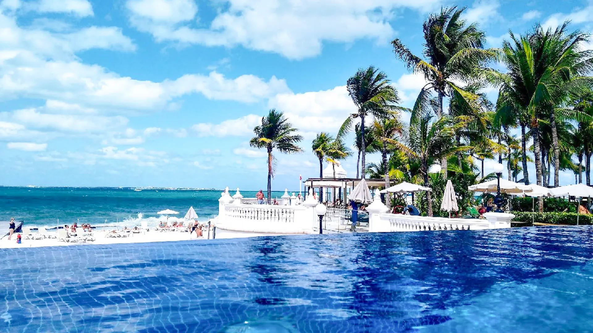 Beachfront infinity pool surrounded by palm trees at Riu Palace Las Americas Cancun.