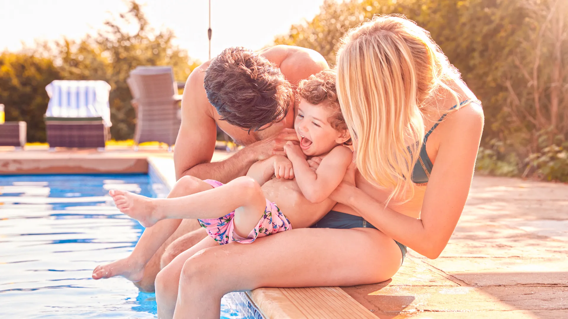 A happy family sitting by the poolside at Royalton Splash Riviera Cancun, parents playing and laughing with their child under the warm Cancun sun.