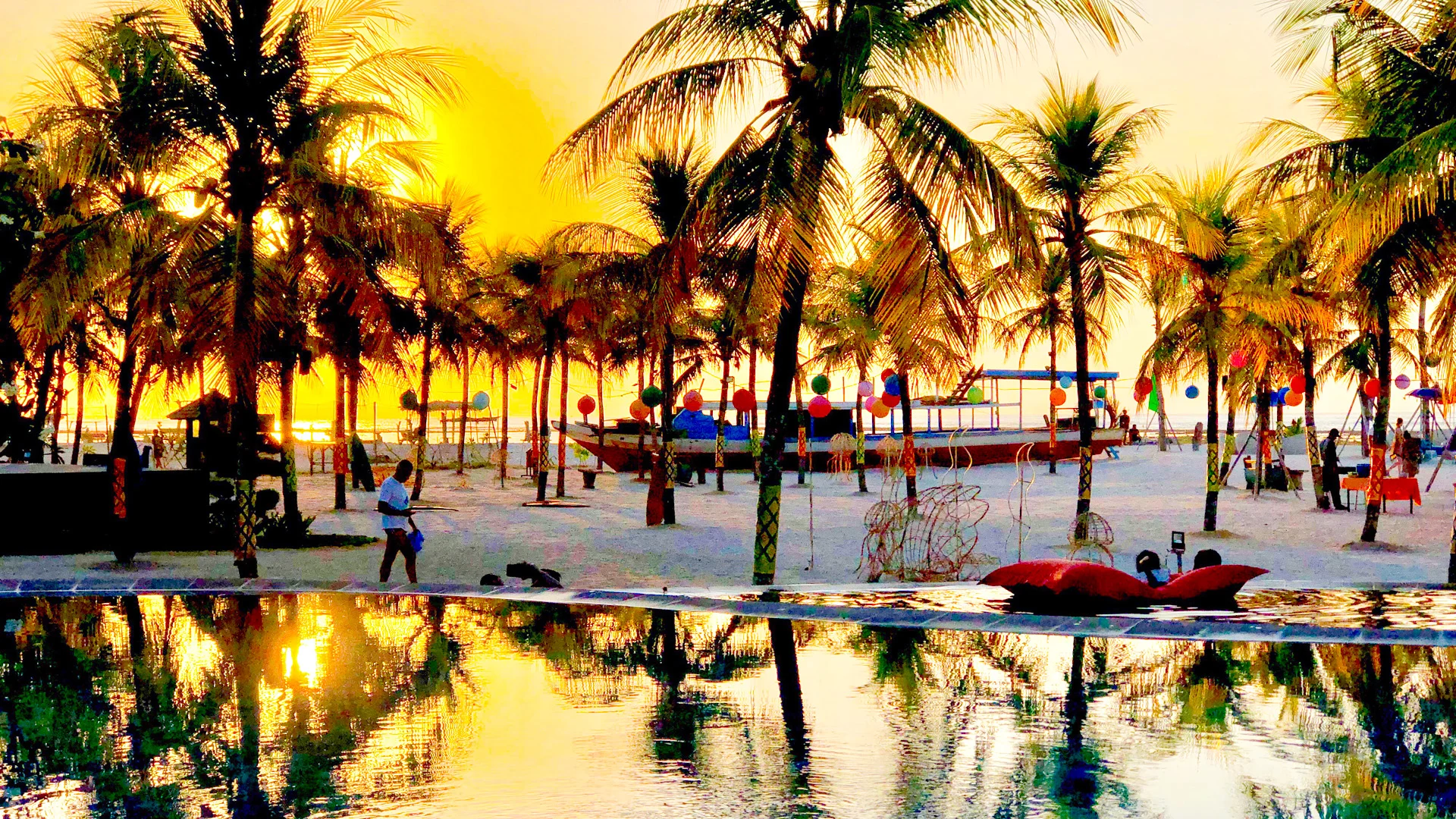 Golden sunset at Temptation Cancun Resort with palm trees reflecting on the pool and beachside boats glowing in warm light. 