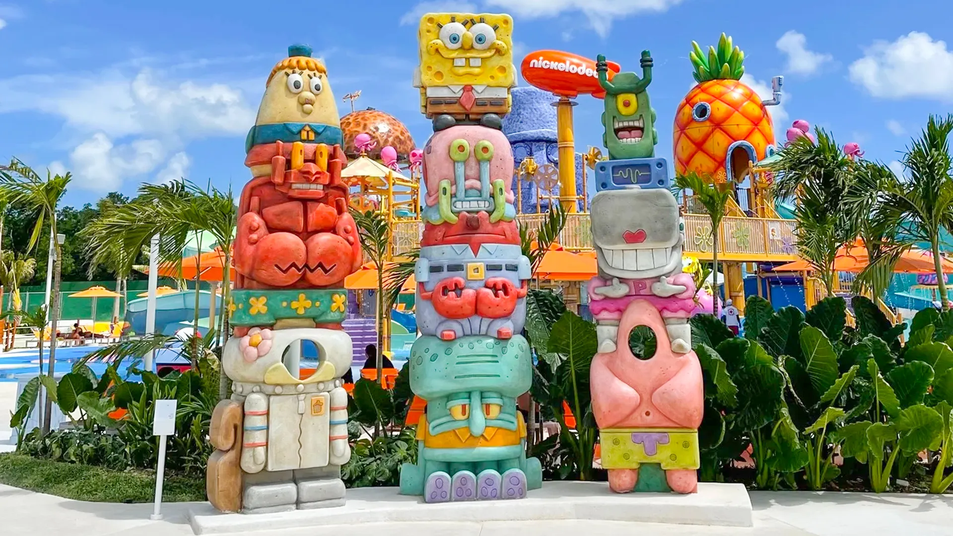 Colorful SpongeBob SquarePants character totem statues at Aqua Nick waterpark in Nickelodeon Resort Cancun, with the pineapple house and slides in the background. 