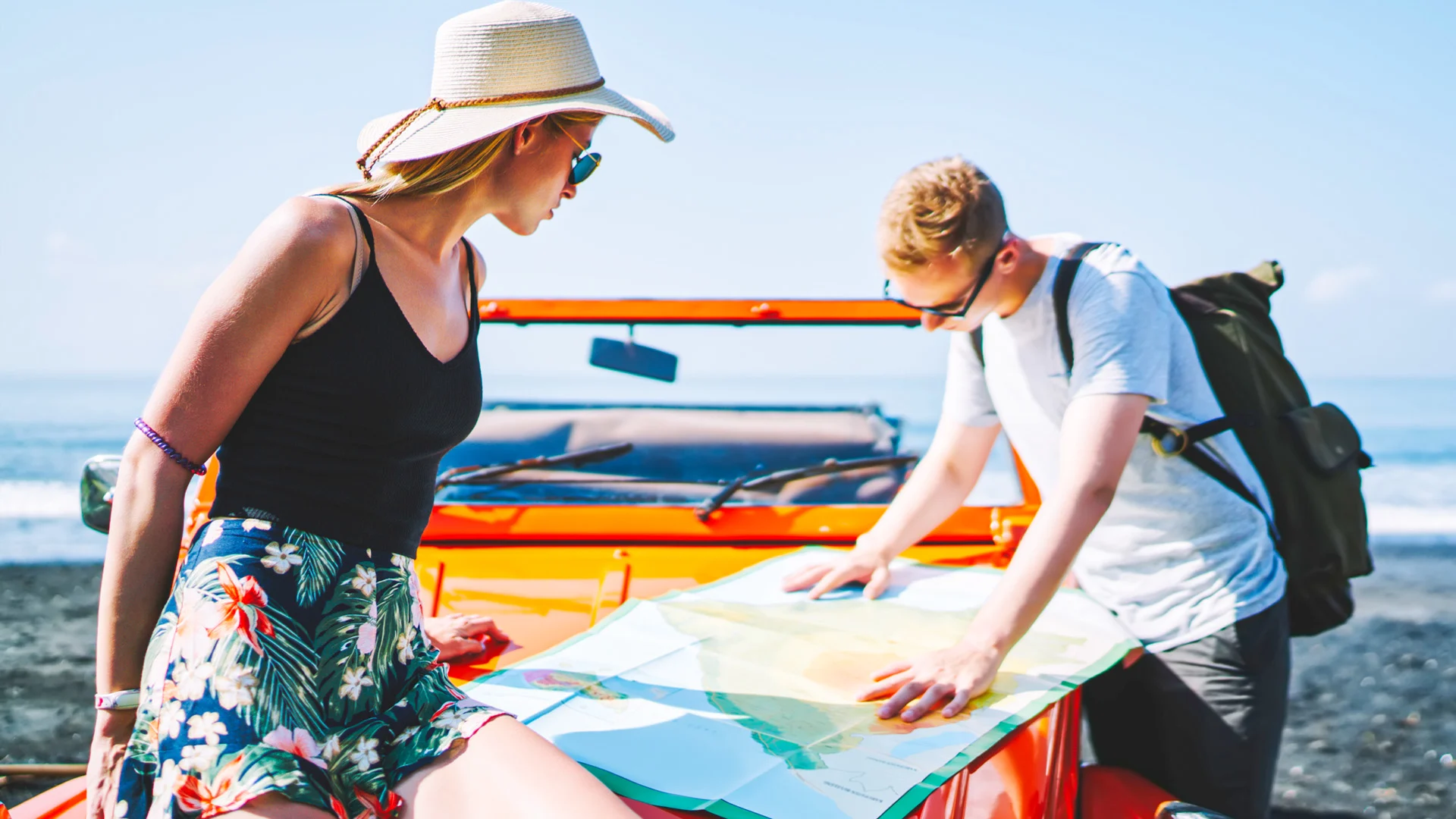 Family sitting together on the beach wearing sun hats, watching the turquoise sea.