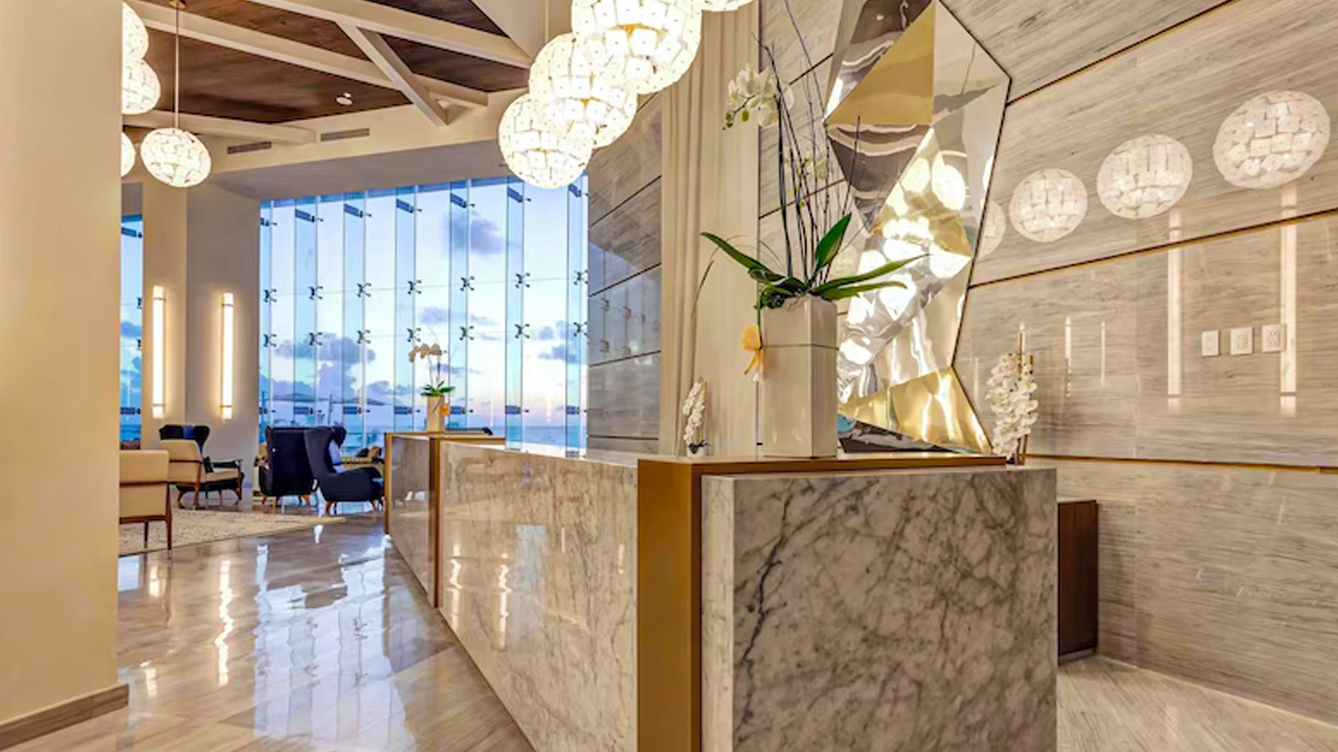 Elegant marble lobby of Royalton Chic Cancun with gold accents, chandeliers, and floor-to-ceiling windows overlooking the sea.