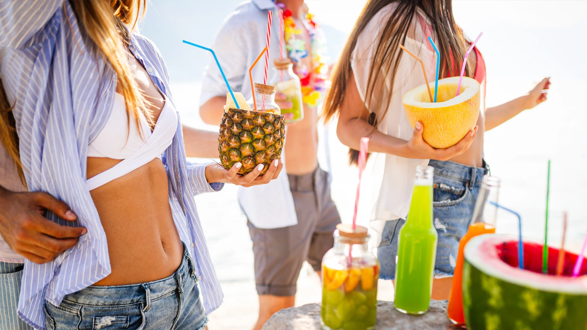 Group of friends at Temptation Cancun beach holding tropical fruit cocktails and colorful drinks.