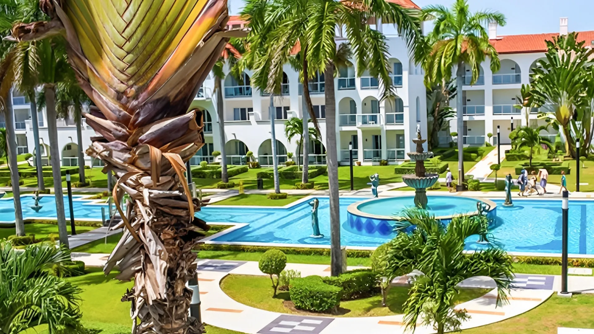 Palm trees and turquoise pools with white colonial-style buildings at Riu Palace Cancun.