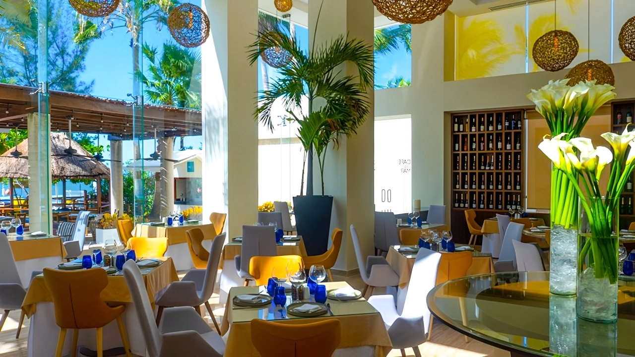 Elegant indoor restaurant at Temptation Cancun Resort with floor-to-ceiling windows, tropical plants, and colorful table settings.