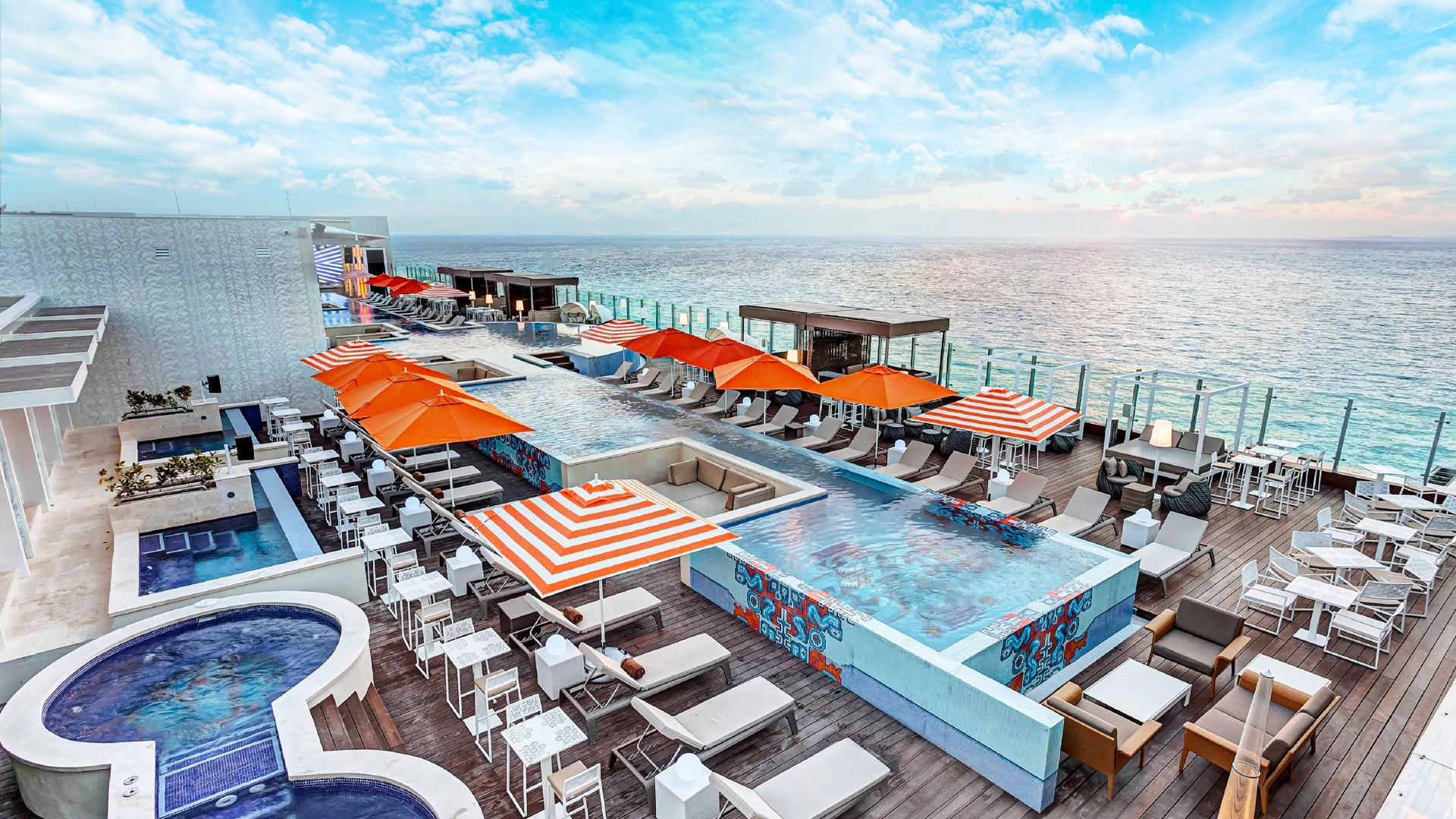 Rooftop infinity pool at Royalton Chic Cancun with orange-striped umbrellas and panoramic ocean views.