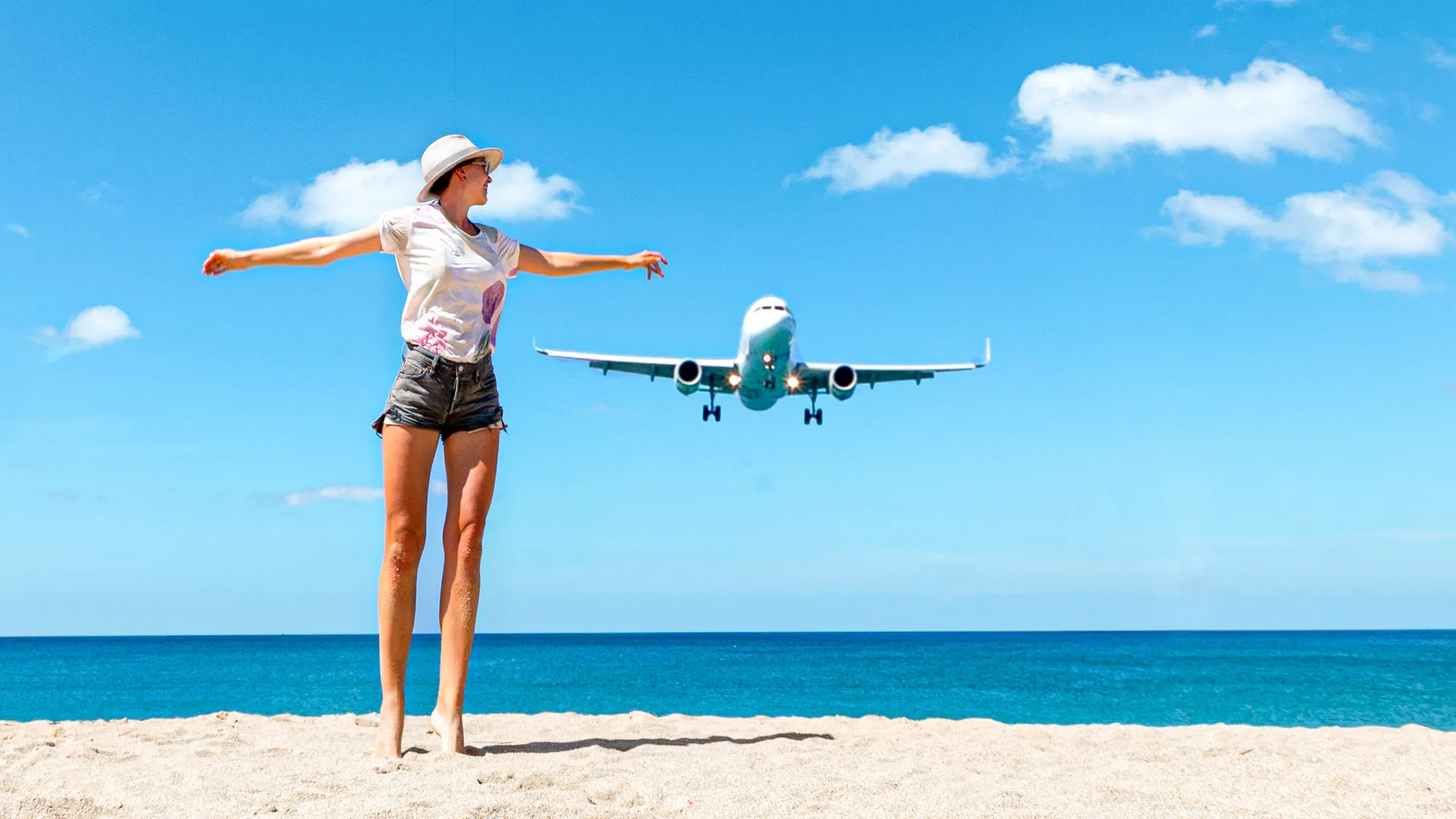  Woman standing on the beach in Cancun with an airplane flying overhead on a sunny day. 
