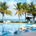 Guests relaxing on in-water loungers surrounded by palm trees at Margaritaville Island Reserve Cancun’s oceanfront pool.