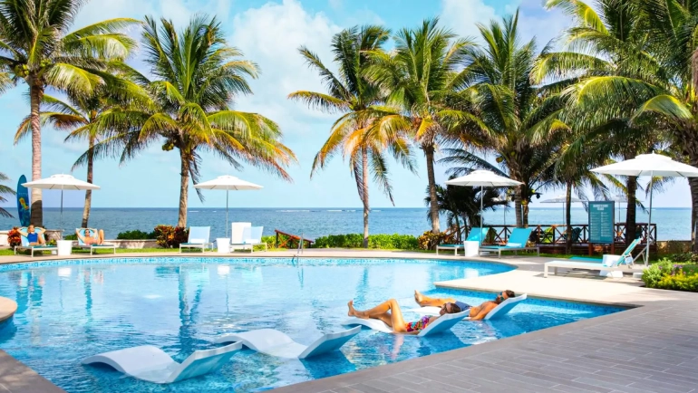 Guests relaxing on in-water loungers surrounded by palm trees at Margaritaville Island Reserve Cancun’s oceanfront pool.