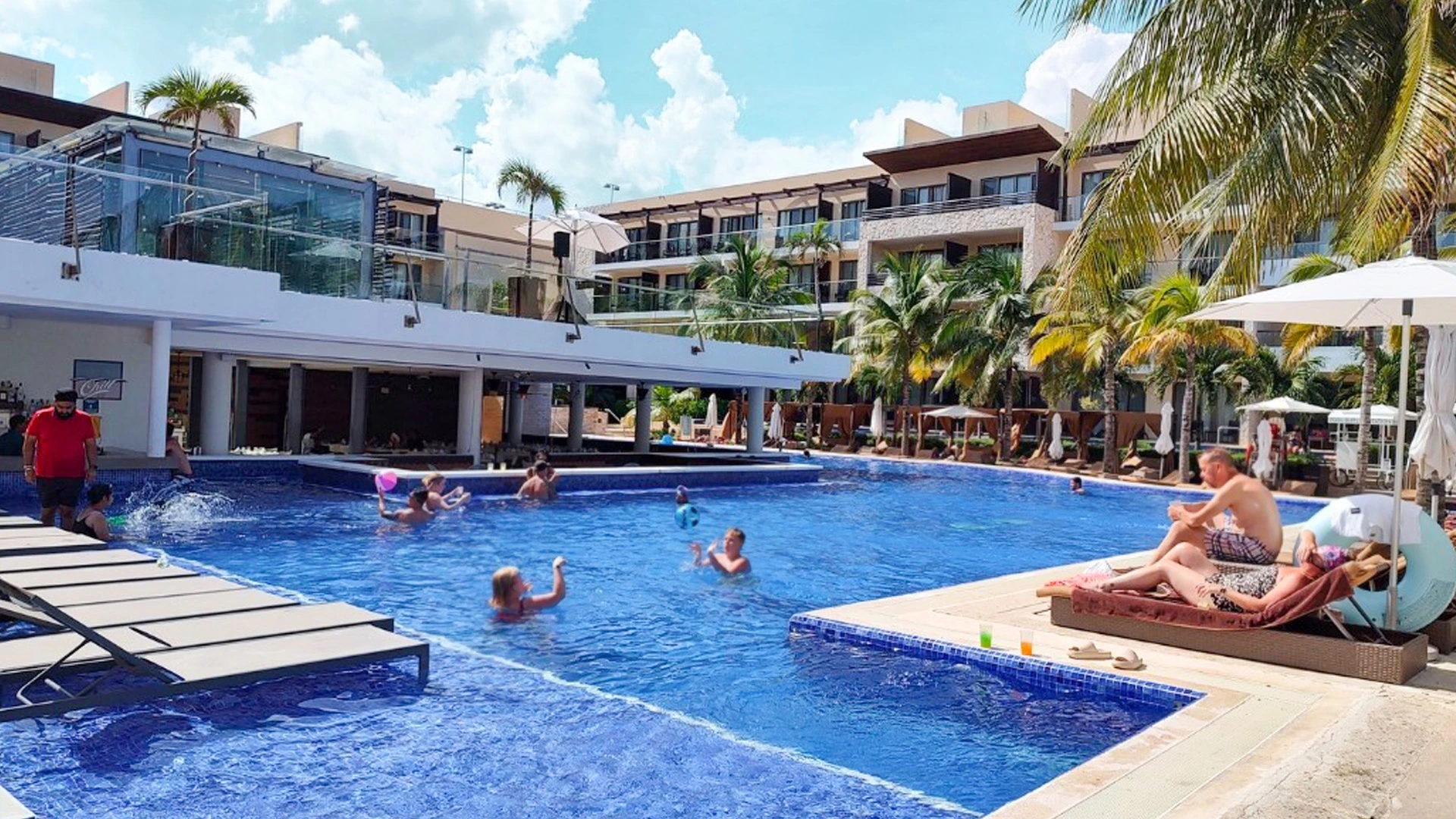 Main pool area at Royalton Chic Cancun with guests enjoying the sun, palm trees, and swim-up bar.