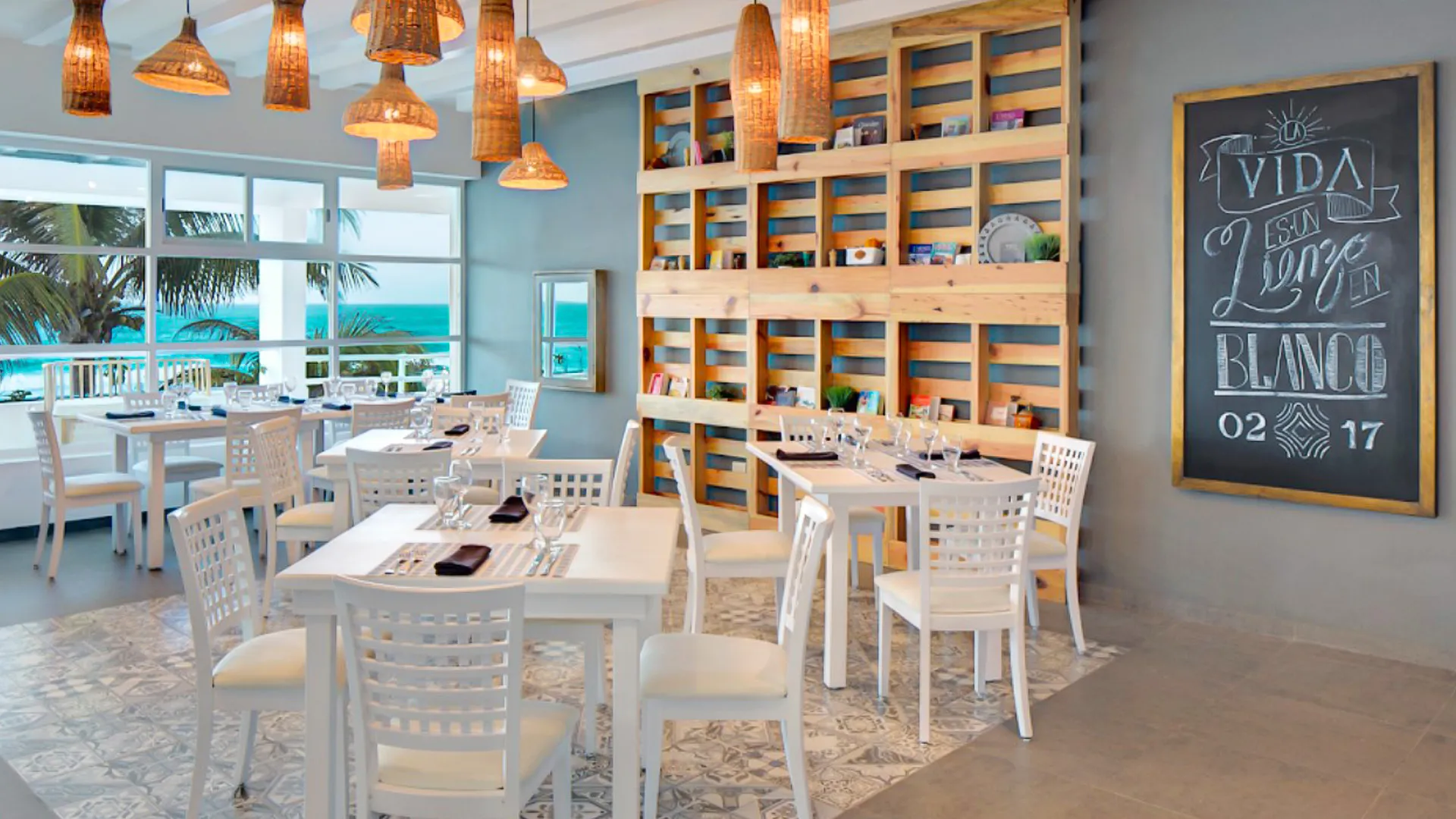 Bright restaurant interior at Oleo Cancun Playa with wooden shelving, chalkboard art, and ocean views.