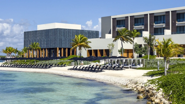 Exterior view of Nizuc Resort Cancun with beachfront cabanas, palm trees, and modern architecture.