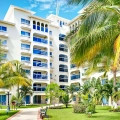 Garden view of Occidental Costa Cancún resort with tropical palm trees, green lawns, and modern white buildings under a bright blue sky.