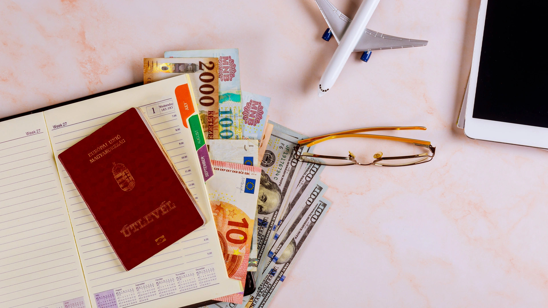 Travel essentials on a desk including passport, international currency, sunglasses, and a miniature airplane.