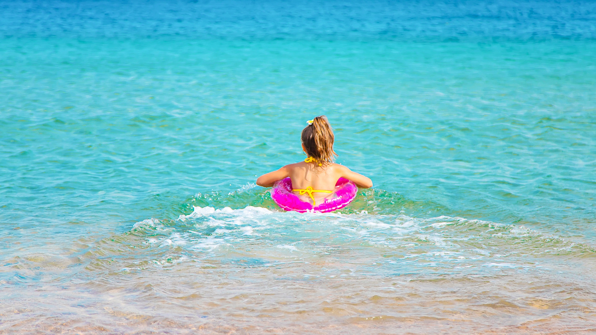 Woman floating in clear turquoise water with a pink swim ring at Temptation Cancun’s beach.