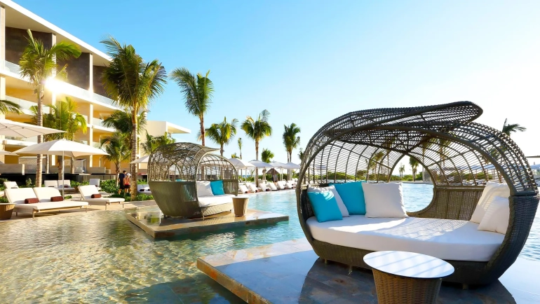 Luxury poolside cabanas with turquoise cushions at TRS Coral Hotel Cancun surrounded by palm trees and modern architecture.