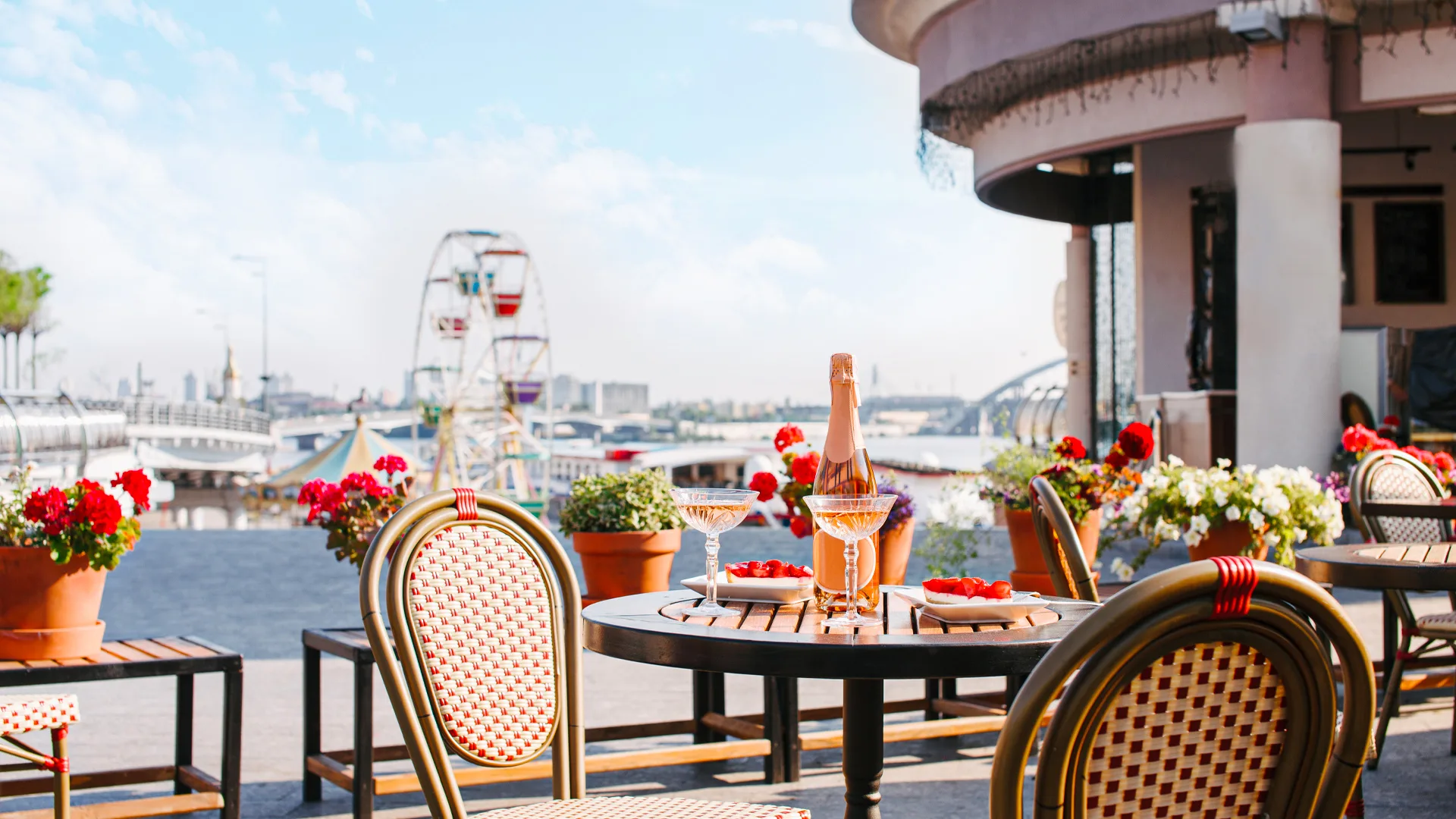 Outdoor café terrace overlooking the waterfront with champagne glasses and blooming flowers on the tables.