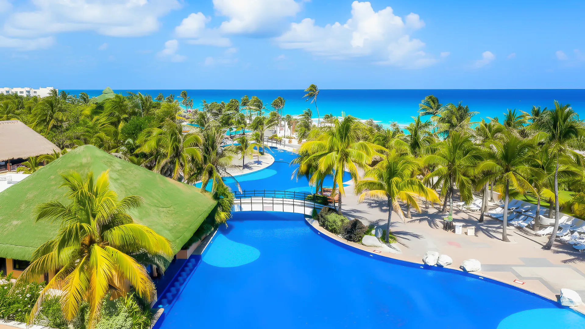  A scenic aerial view of the Grand Oasis Cancun, showcasing the lush palm trees and vibrant blue swimming pool with the beautiful beach in the background.
